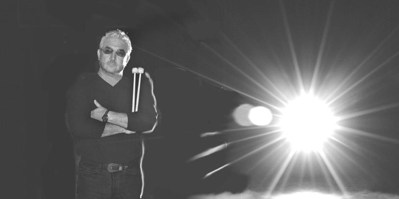 Black and white photo of a man with drumsticks and bright light.