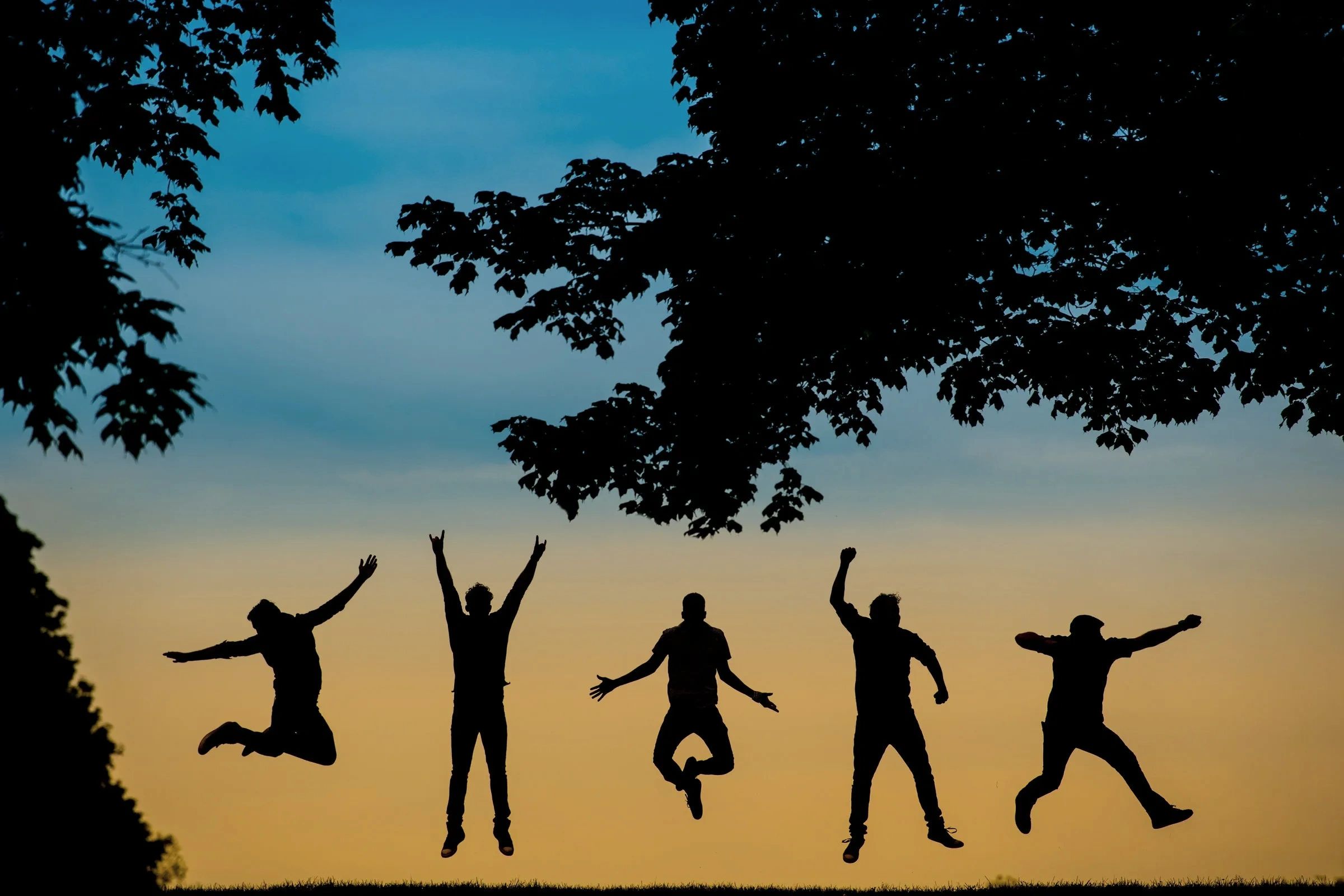 Five band members in silhouette at sunset appear to be floating because they were captured mid-jump.