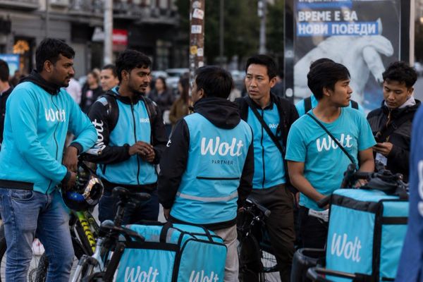 Delivery workers in blue Wolt uniforms gather with bicycles and delivery bags.