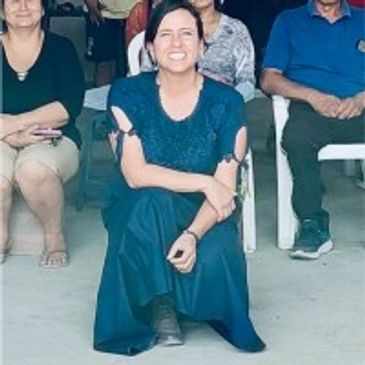 A woman in a blue dress smiling while sitting on the floor among seated people.