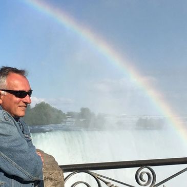 Man in sunglasses admires a rainbow over a waterfall.
