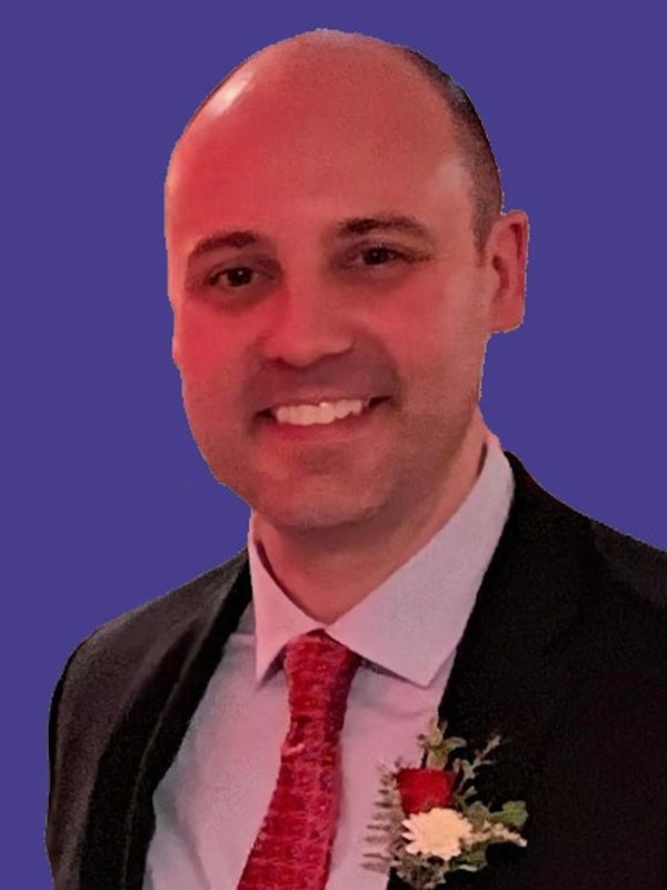 Smiling man in suit and red tie with boutonniere.