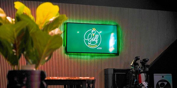 Indoor golf lounge with illuminated Golf Gardens sign and golf clubs.