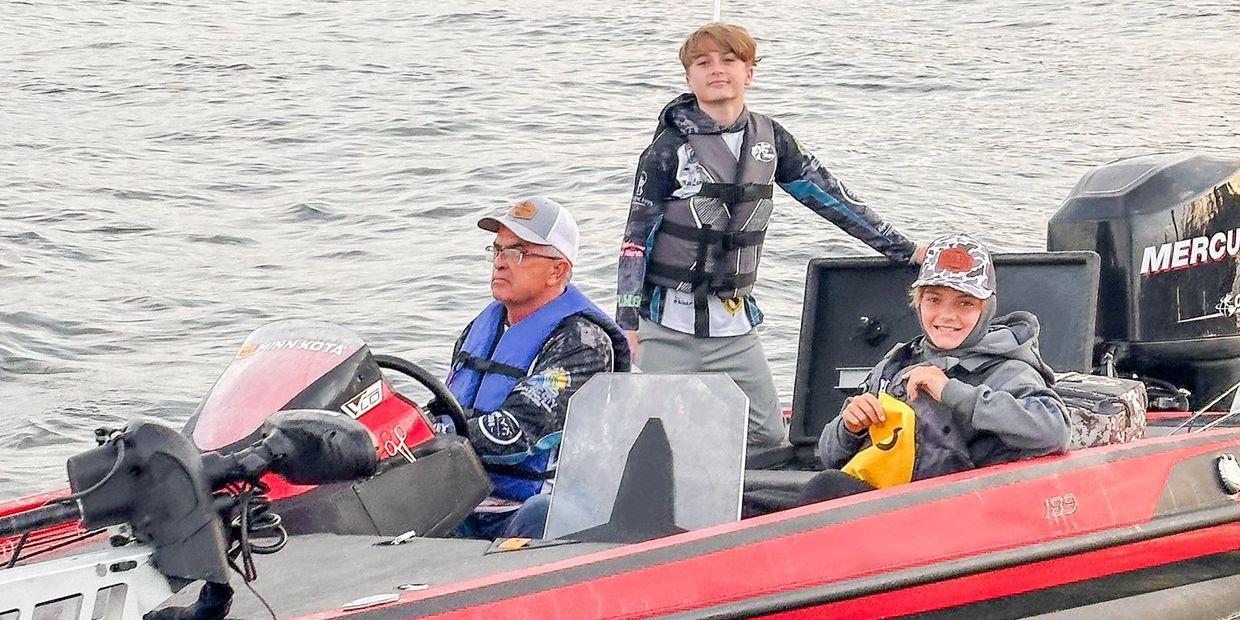 Three people on a red fishing boat on the water, wearing life jackets.