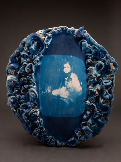 Blue ceramic artwork featuring a vintage-style portrait surrounded by intricate curls.
