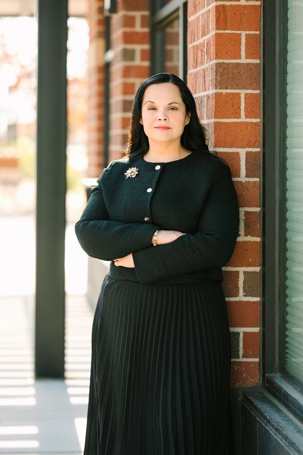 Woman in black outfit standing confidently against a brick wall.