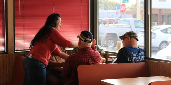 A waitress serves three men seated in a diner booth near a window.