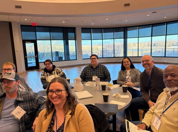 Group of professionals smiling around a table in a bright meeting room.