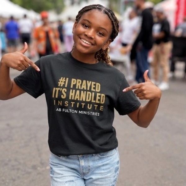 Young girl proudly pointing to her inspirational message T-shirt at an outdoor event.