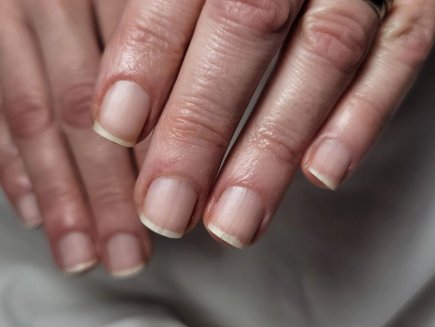 Close-up of natural, well-kept fingernails on slightly wrinkled hands.