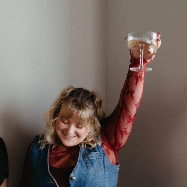 Woman happily raising a glass in celebration, smiling with eyes closed.