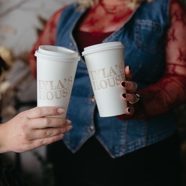 Two hands holding coffee cups with 'LYLA'S HOUSE' printed on them.