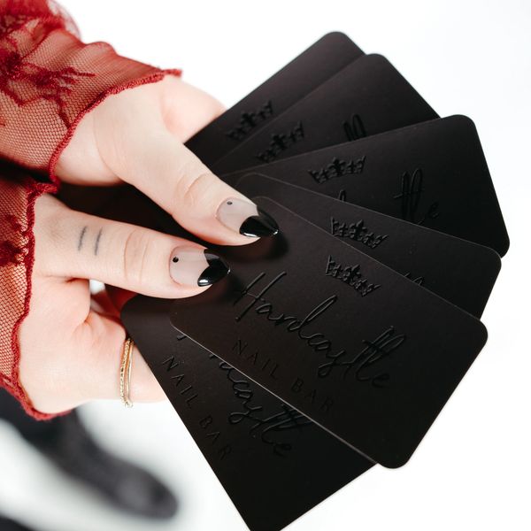 Hand holding black business cards for Hardcastle Nail Bar with stylish nail art.