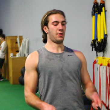 Man exercising in gym wearing gray tank top.