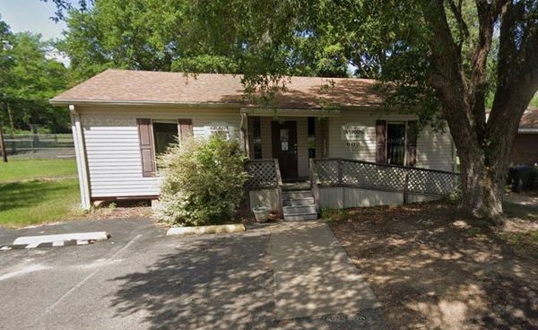 Small white building with a ramp and a tree in front.