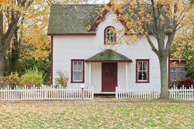 Small white house with a red door and autumn foliage.