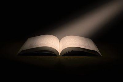 Open book illuminated by a focused light beam in darkness.