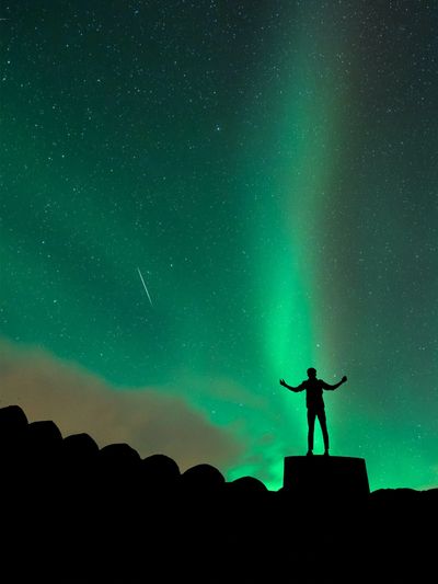 Silhouette watching the northern lights under a starry sky.
