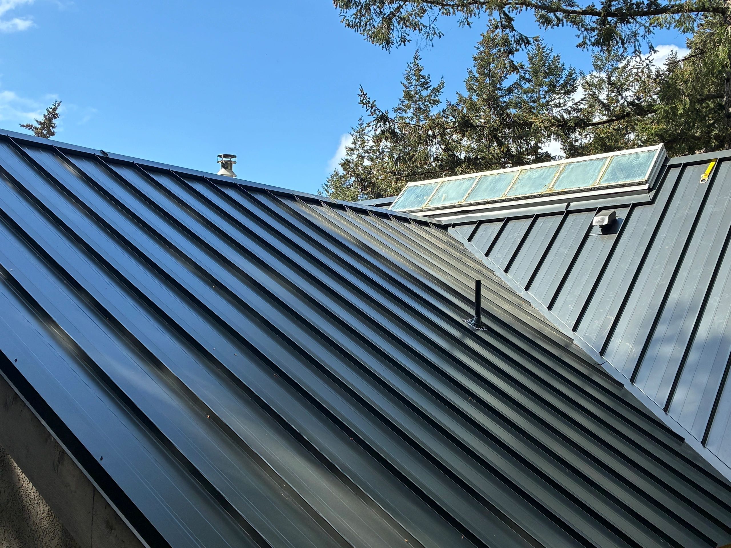 Modern metal roof with skylight panels under a clear blue sky.