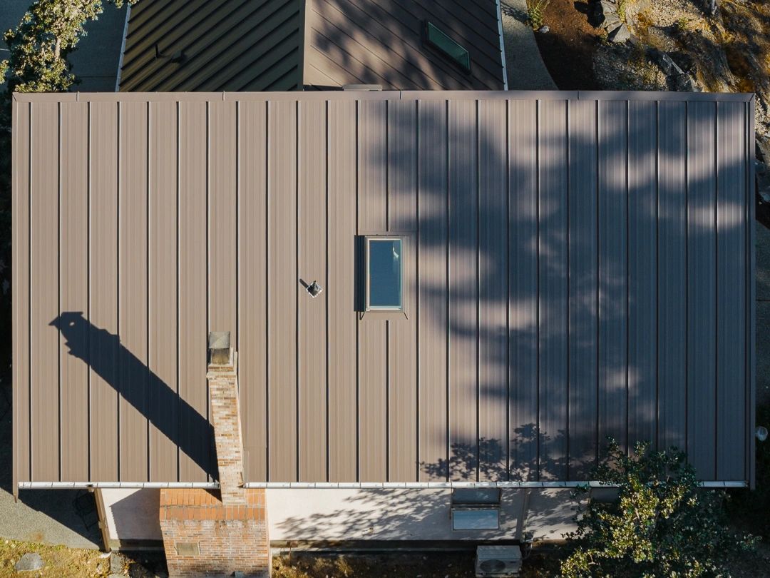 Aerial view of a house with a metal roof and chimney casting a shadow.