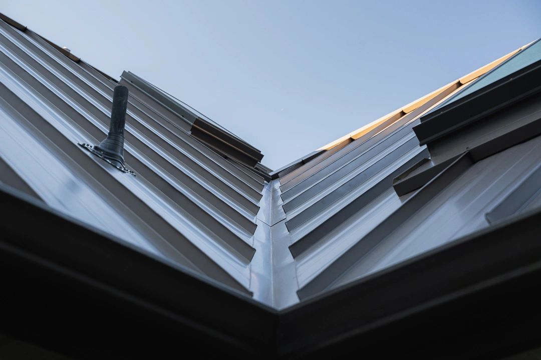 Close-up of a metal roof with a vent pipe under clear sky.