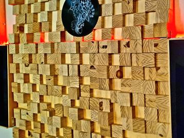Wooden acoustic panel with varied block depths and a black circular logo.