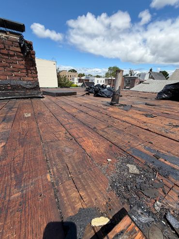 Worn wooden rooftop with chimney under a blue sky.