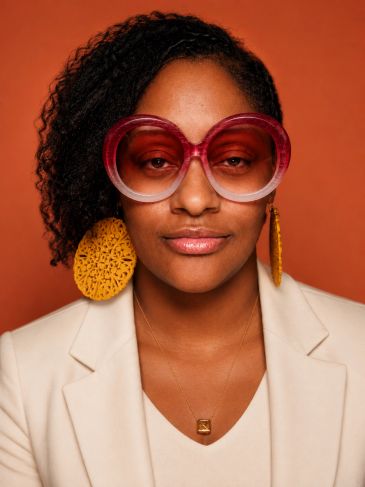 Woman with large pink sunglasses and yellow earrings.