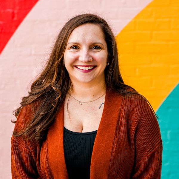 Ashley Scheetz standing in front of a vibrantly colored wall smiling.