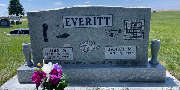 Gravestone of John M. and Janice M. Everitt with engraved symbols and flowers.
