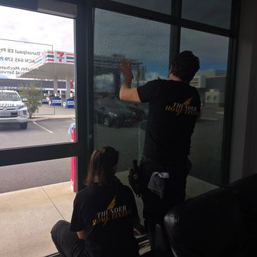 Two workers applying film to a glass door.