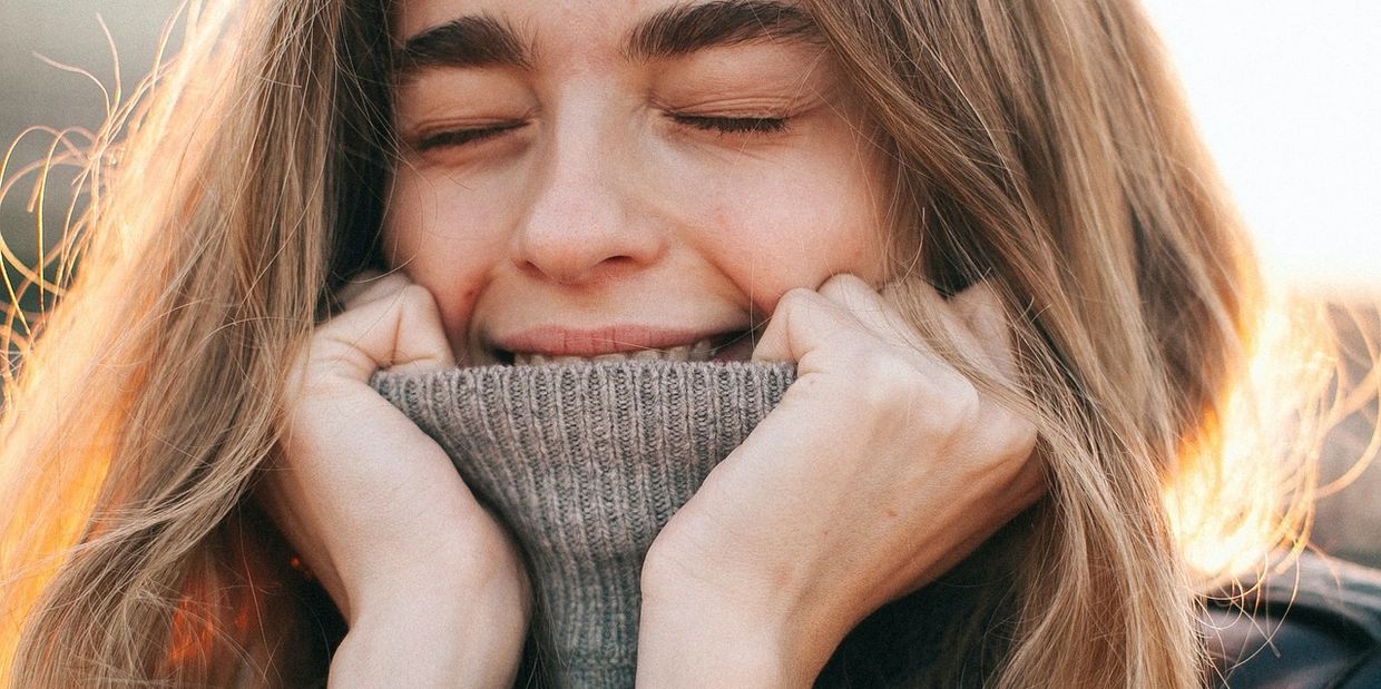 A woman smiling warmly with eyes closed, holding a cozy sweater near her face.