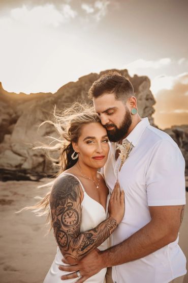 Couple embracing on a beach at sunset with warm lighting.