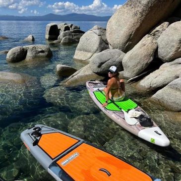 Person on paddleboard among large rocks in clear water.