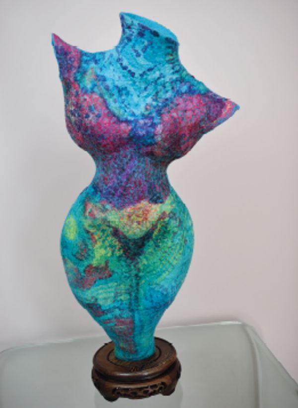 Colorful abstract sculpture of a female torso on a wooden base.
