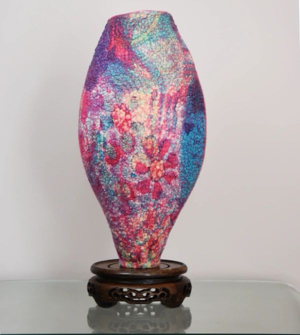 Colorful textured vase on an ornate wooden stand.