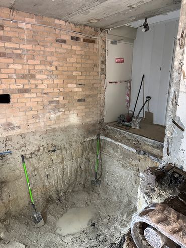 Excavation site indoors with shovels and brick wall.