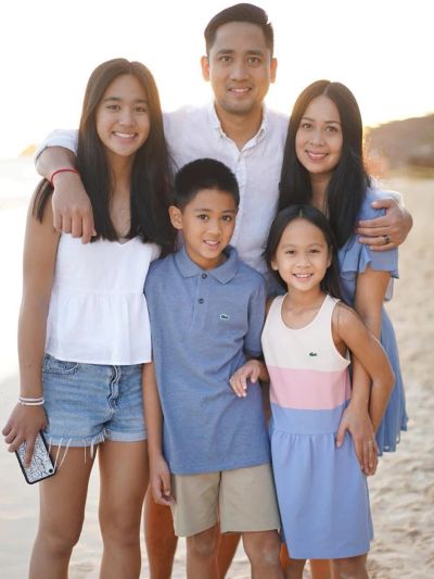 Smiling family of five posing on the beach at sunset.