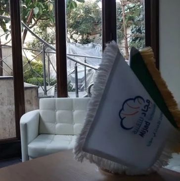A white armchair near a window with flags on a table.