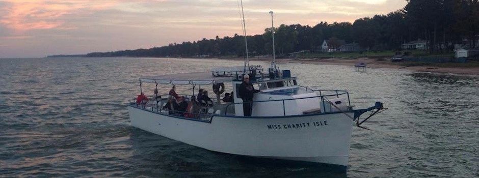 Boat named Miss Charity Isle on calm waters near shore at sunset.