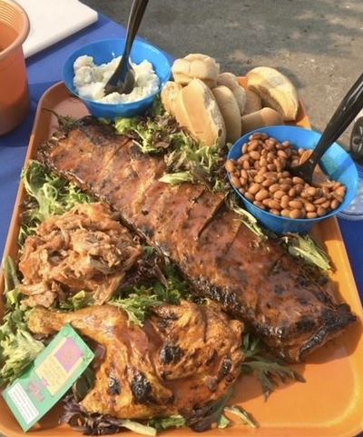 Barbecue ribs, chicken, beans, bread, and sides on a tray.