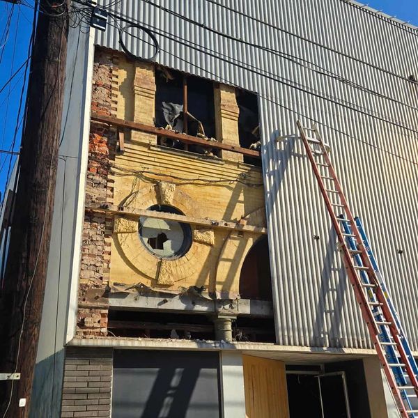 Old building facade partially exposed behind modern metal siding with ladders leaning against it.