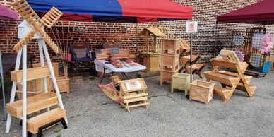Outdoor market stall selling wooden crafts and decorations under a red and blue canopy.