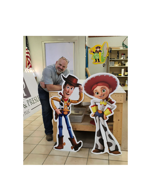 Man posing with Woody and Jessie cutouts from Toy Story.