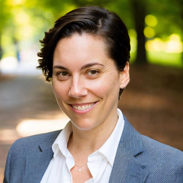 White woman with dark hair wearing a white shirt and blue blazer, looking at camera and smiling.