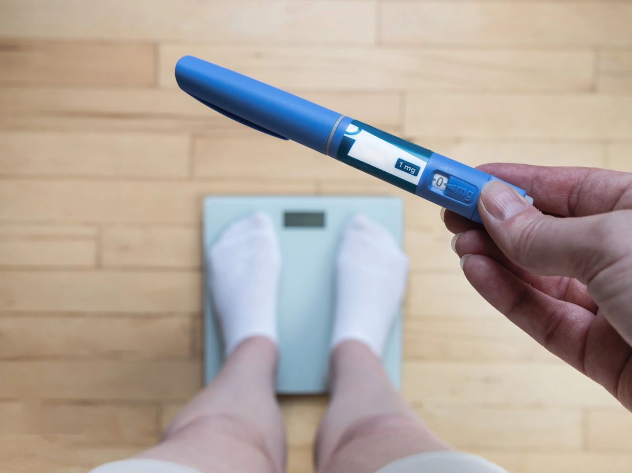 Hand holding insulin pen with feet on scale in background.