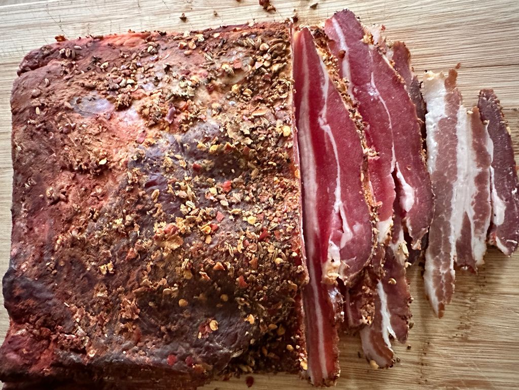 Sliced spiced cured meat on a wooden cutting board.