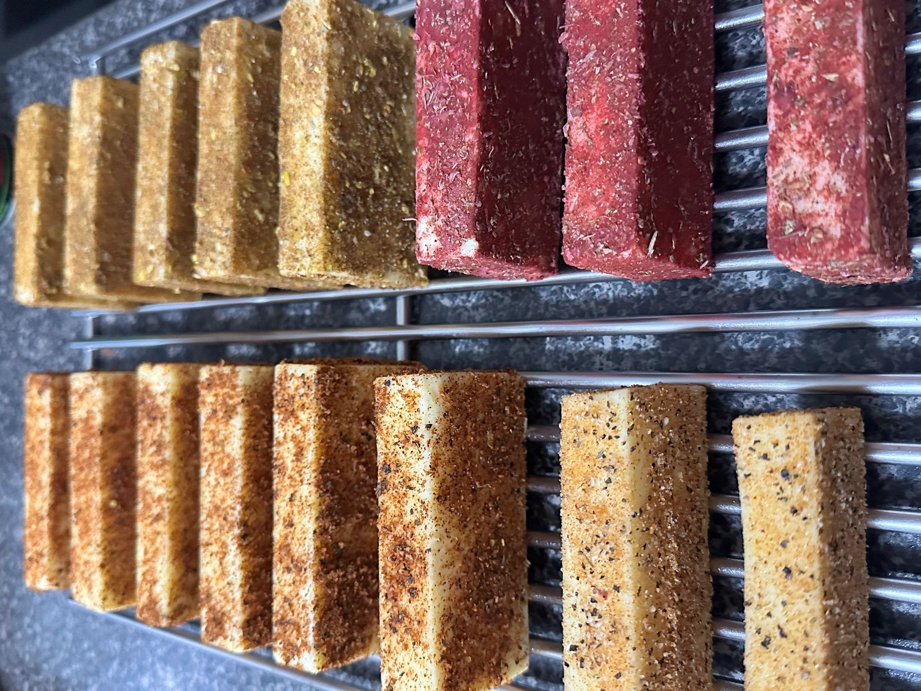 Colorful spice-coated blocks drying on a metal rack.