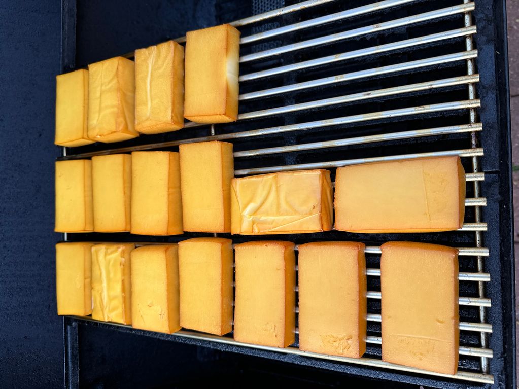 Multiple blocks of cheese smoking on a grill rack.