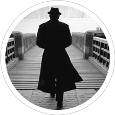 Man wearing a hat and a long coat walking on a bridge